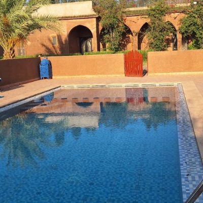 Image photo d'un riad marocain avec au premier plan la pisicine, au fond, le riad entouré des oliviers